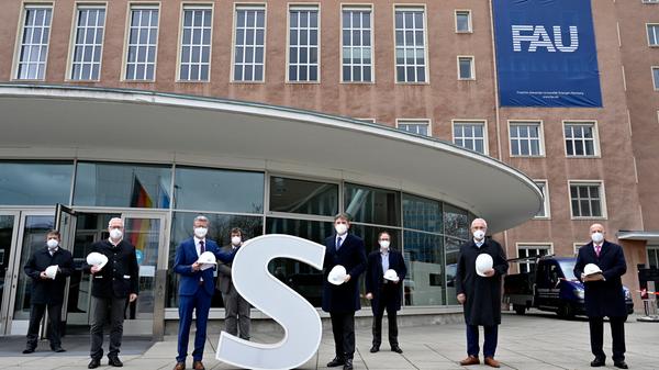 Bereits im Dezember wurden die Schlüssel zum Erlanger „Himbeerpalast“ von der Siemens AG an die FAU übergeben – nun hat die Universität das Gebäude ganz offiziell übernommen. Um die Übergabe auch nach außen hin sichtbar zu markieren, wurde während des Termins symbolisch der erste Buchstabe des Siemens-Schriftzugs vom Gebäude entfernt – in Zukunft ist dann Platz für das FAU-Logo.