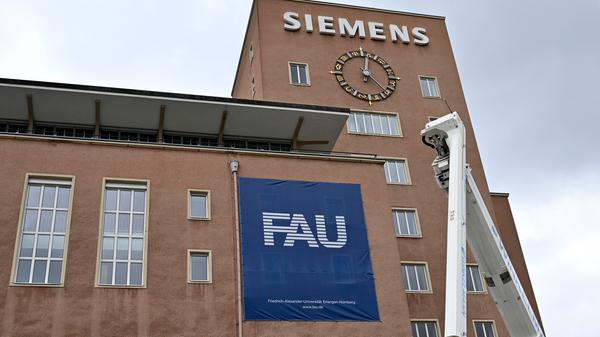 Bereits im Dezember wurden die Schlüssel zum Erlanger „Himbeerpalast“ von der Siemens AG an die FAU übergeben – nun hat die Universität das Gebäude ganz offiziell übernommen. Um die Übergabe auch nach außen hin sichtbar zu markieren, wurde während des Termins symbolisch der erste Buchstabe des Siemens-Schriftzugs vom Gebäude entfernt – in Zukunft ist dann Platz für das FAU-Logo.