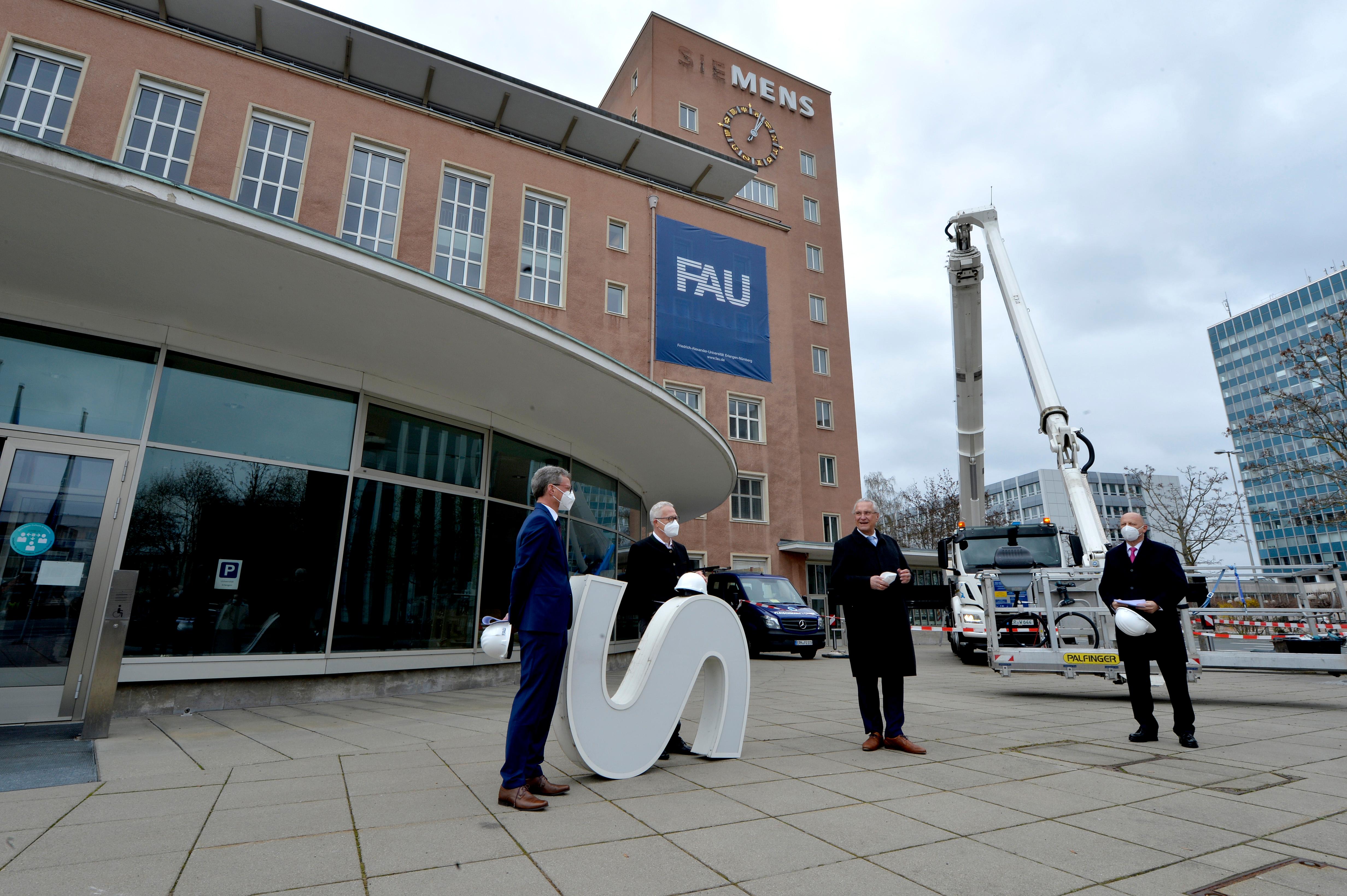 Bereits im Dezember wurden die Schlüssel zum Erlanger „Himbeerpalast“ von der Siemens AG an die FAU übergeben – nun hat die Universität das Gebäude ganz offiziell übernommen. Um die Übergabe auch nach außen hin sichtbar zu markieren, wurde während des Termins symbolisch der erste Buchstabe des Siemens-Schriftzugs vom Gebäude entfernt – in Zukunft ist dann Platz für das FAU-Logo.