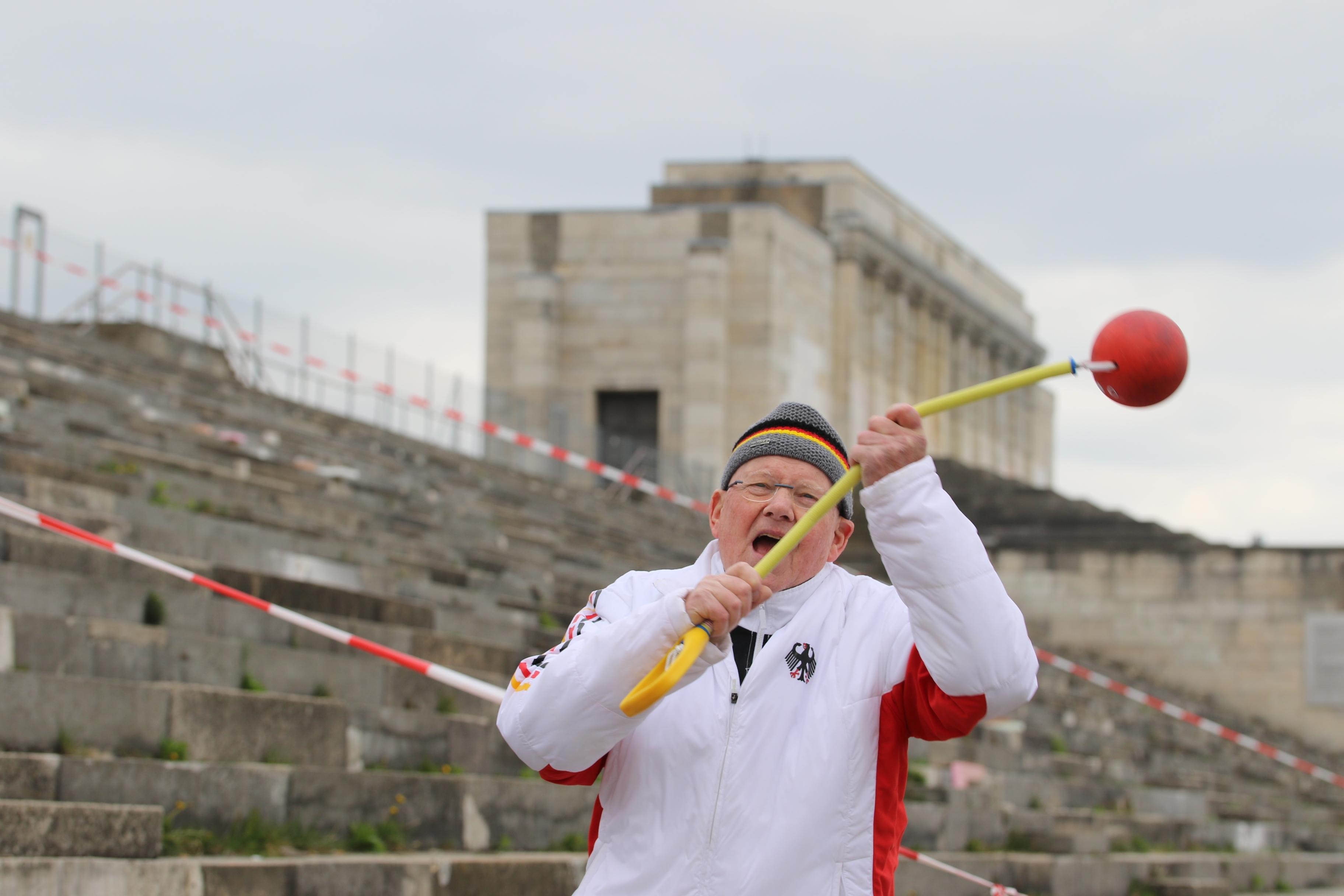 Auch mit 80 Jahren ist Dietmar Keller noch topfit. Er stößt die Kugel, wirft den Hammer (hier vor der Nürnberger Steintribüne) oder den Speer und unterstützt seinen Bekannten Achim Sanftleben mit seiner jahrzehntelangen Erfahrung als Trainer. Die beiden fahren "gemeinsam zu nationalen, internationalen Meisterschaften und wollen bei unseren Reisen nach Polen, Ungarn, Spanien, Österreich usw. noch ein wenig von unserem arbeitsreichen Leben mit Lebensfreude ausklingen lassen".