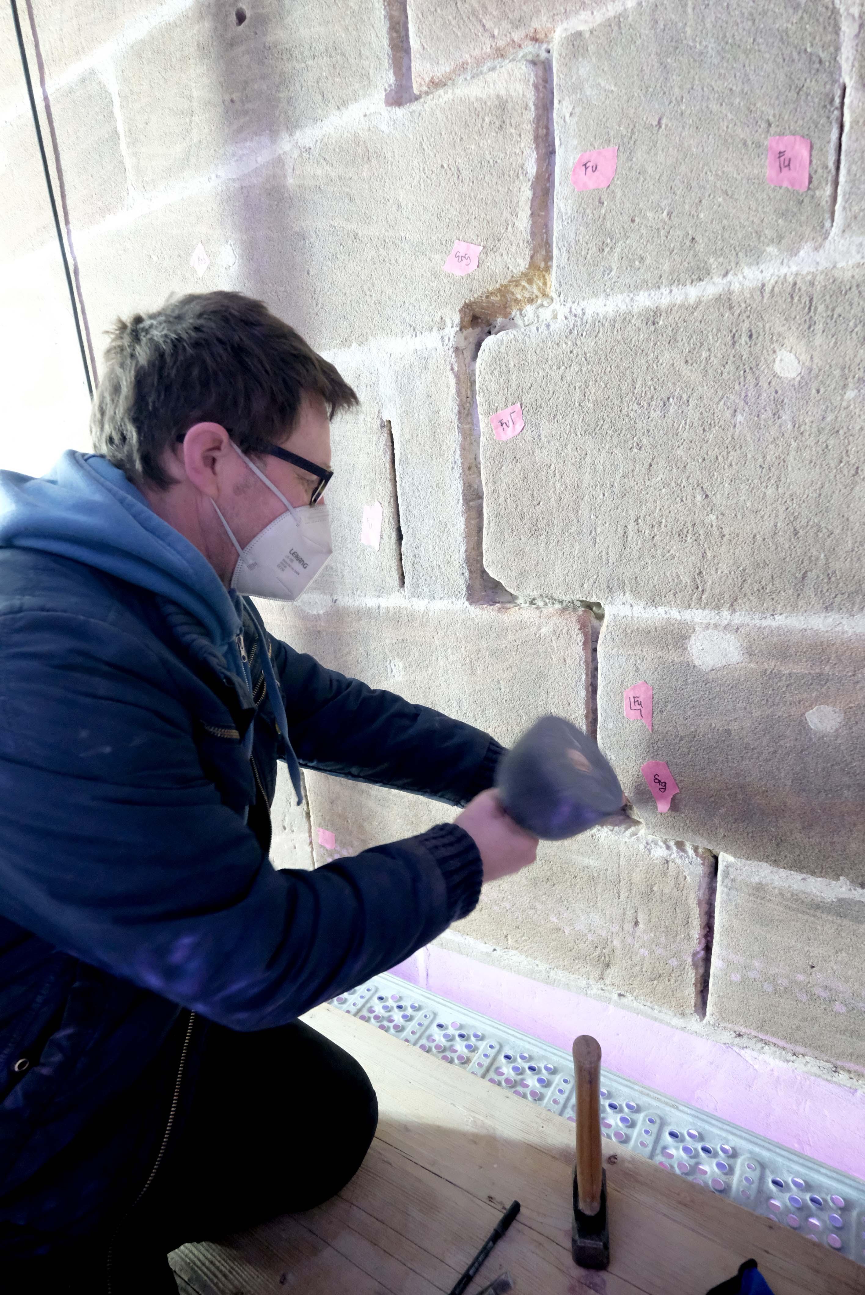 Ein Steinmetz stemmt eine Sandsteinfuge aus.