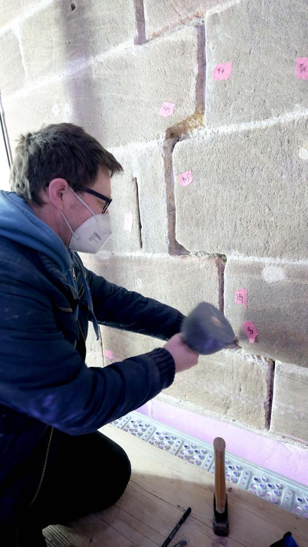 Ein Steinmetz stemmt eine Sandsteinfuge aus.