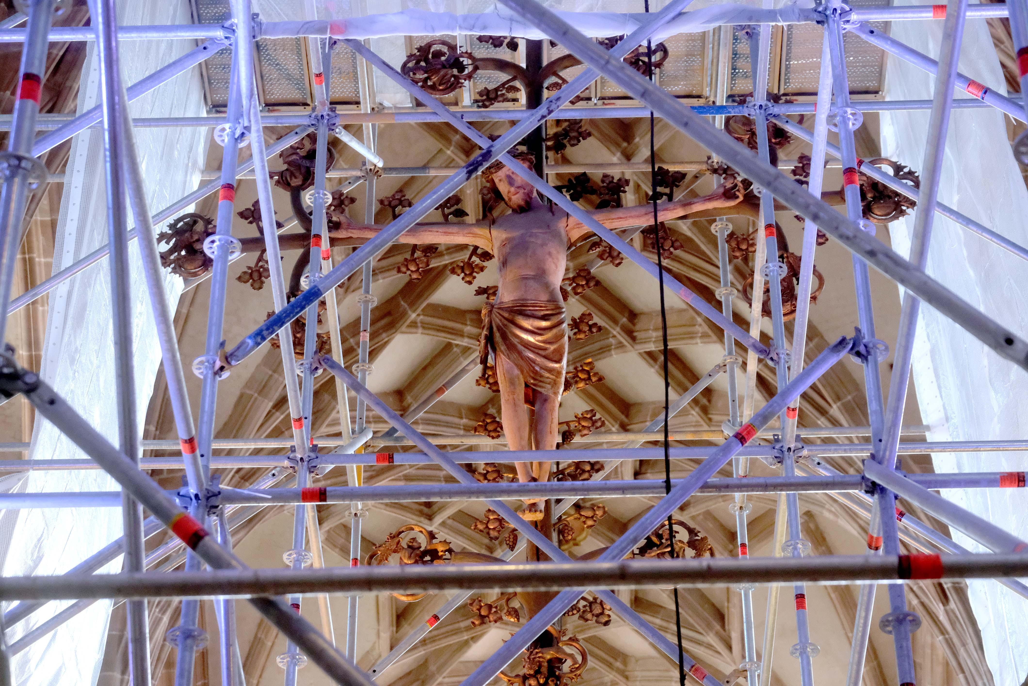 Wie eine Kunstinstallation: Durch Gerüststangen blickt man auf den gekreuzigten Christus.