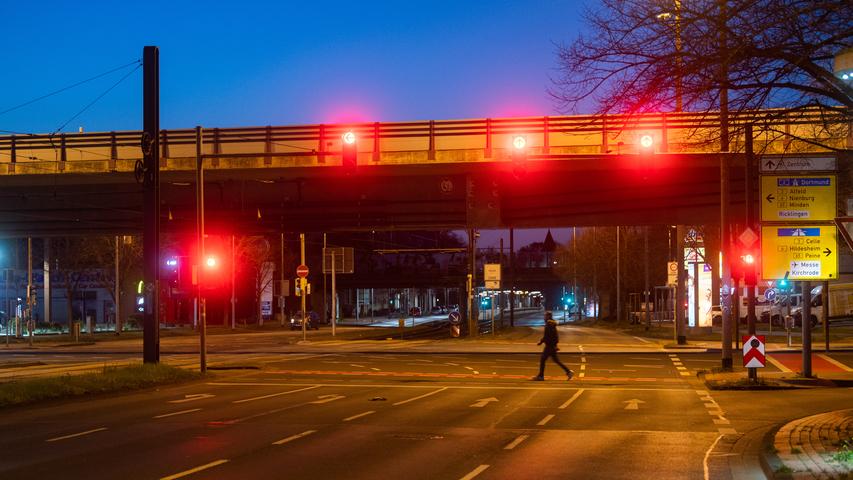 Rote Ampel leuchten auf der leeren Hildesheimer Straße, als ein einzelner Passant die Straße überquert. Das neue Infektionsschutzgesetz sieht wegen der Corona-Pandemie eine bundeseinheitliche nächtliche Ausgangssperre in Regionen mit einer Sieben-Tage-Inzidenz über 100 vor.