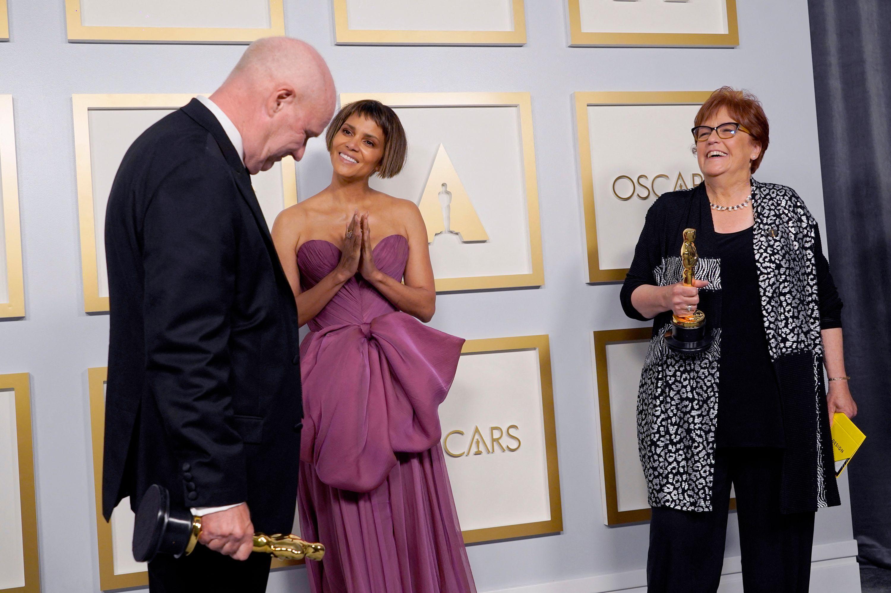Donald Graham Burt (l), Artdirector, und Jan Pascale (r), Szenenbildnerin, posieren im Presseraum mit dem Oscar für das beste Produktionsdesign für "Mank" mit Schauspielerin Halle Berry.