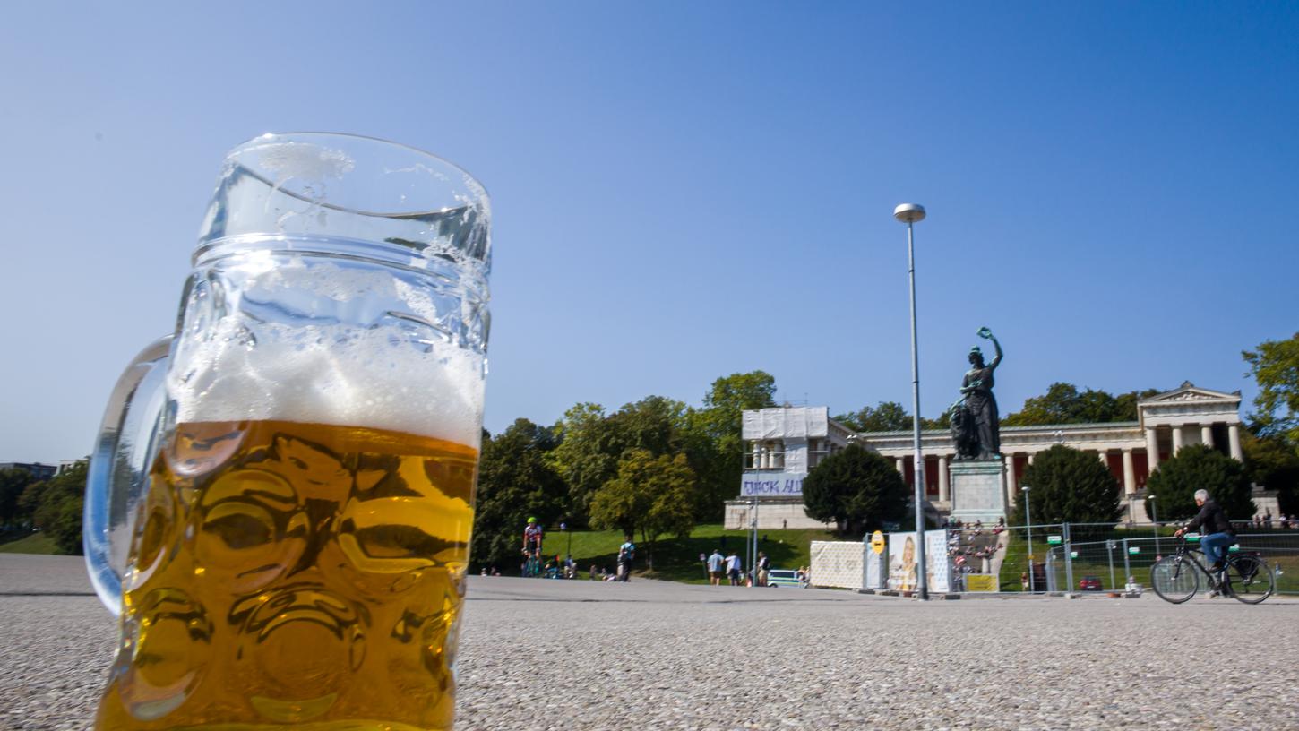 Ein verlassener, halb gefüllter Bierkrug steht auf dem Wiesn-Gelände auf dem Asphalt. Im Hintergrund ist die Bavaria-Statue zu sehen. Wegen der Corona-Pandemie wurde das Oktoberfest erneut abgesagt.