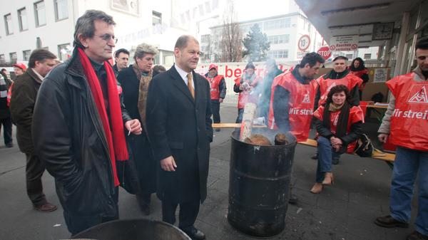 Von 2007 bis 2009 bekleidete Olaf Scholz das Amt des Bundesministers für Arbeit und Soziales in der Großen Koalition unter Bundeskanzlerin Angela Merkel. Er folgte auf Parteigenosse Franz Müntefering, der sich aus familiären Gründen aus dem Amt zurückzog. Hier besuchte er den AEG-Streik in Nürnberg mit Lizzy Gröhner und Martin Burkert.