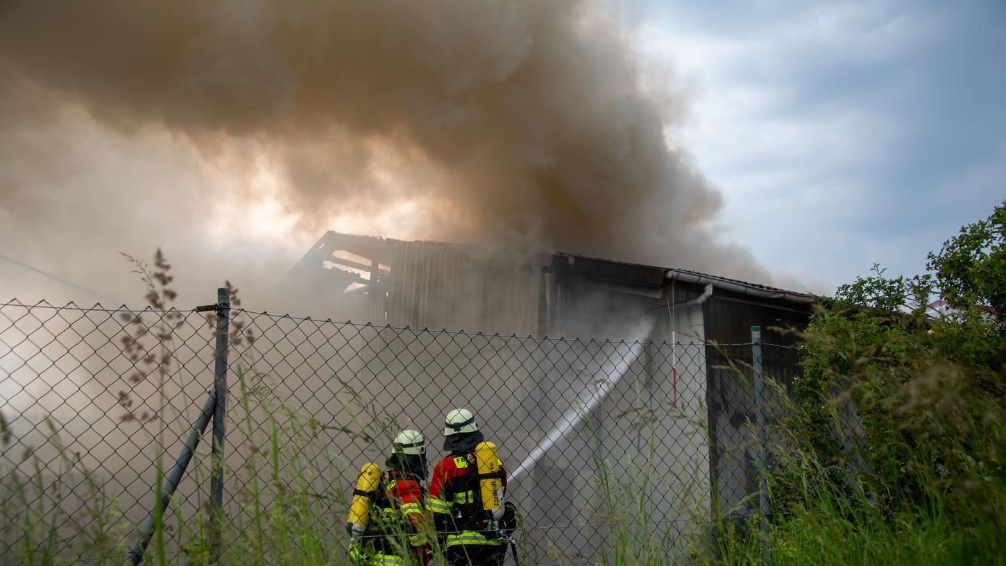 Feuerwehrleute löschen eine brennende Lagerhalle auf dem Gelände eines Entsorgungsbetriebes.