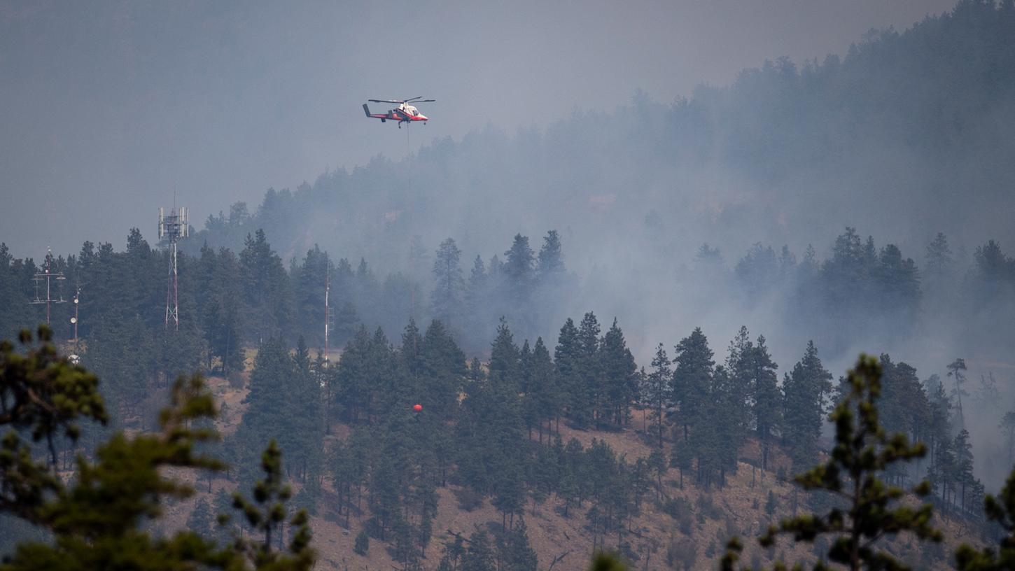 Ein Hubschrauberpilot bereitet sich darauf vor, Wasser auf ein brennendes Waldfeuer in Lytton, British Columbia, abzuwerfen.