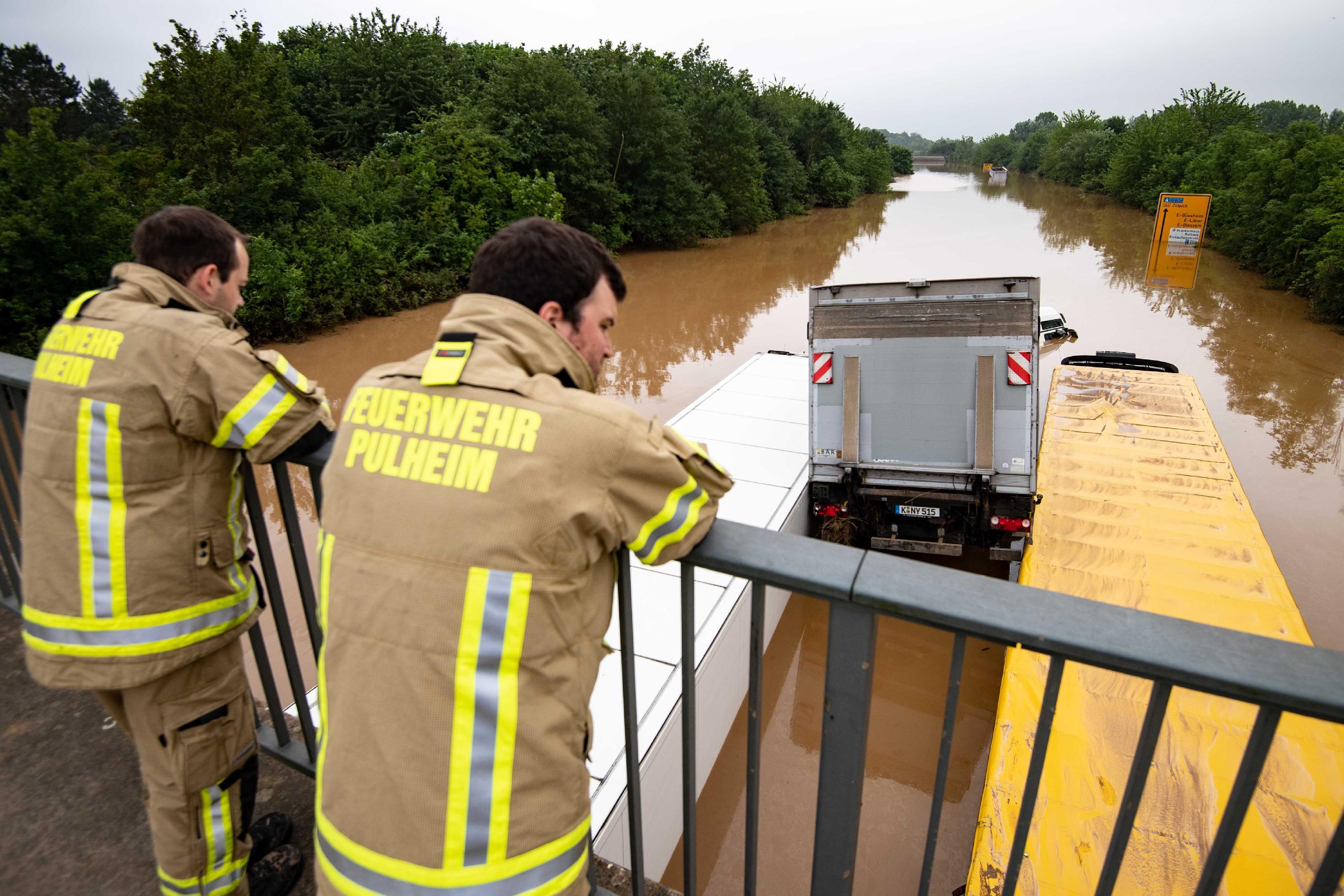 Die B265 bei Erftstadt ist völlig überflutet. Feuerwehrmänner blicken auf ineinander verkeilte LKWs. 