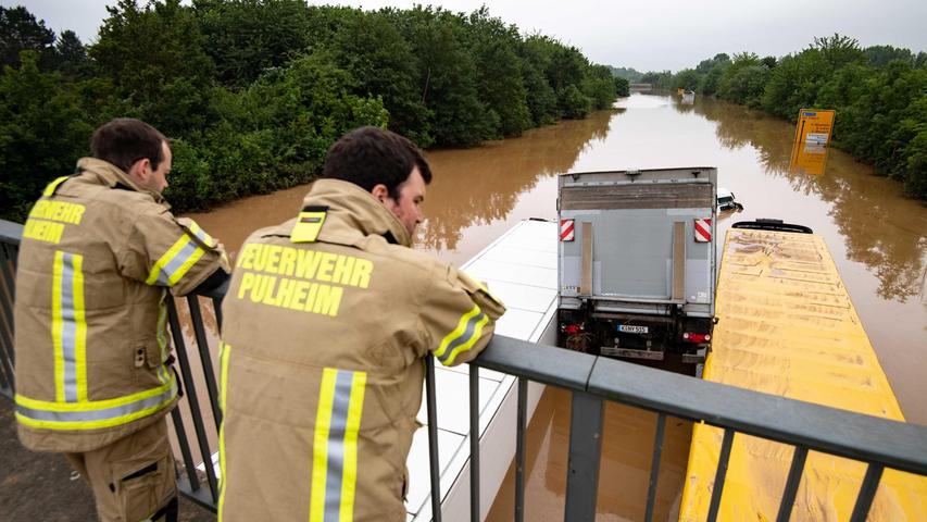 Die B265 bei Erftstadt ist völlig überflutet. Feuerwehrmänner blicken auf ineinander verkeilte LKWs. 