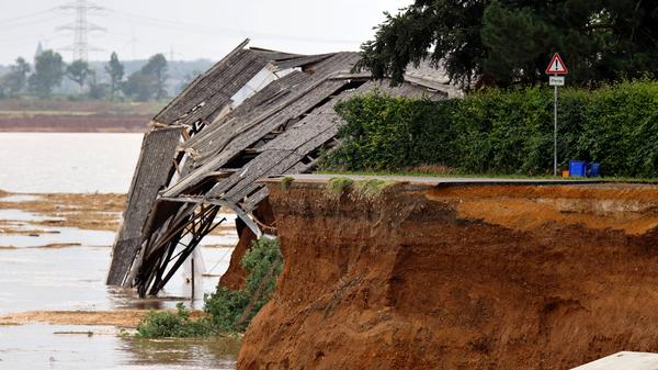 In Erftstadt-Blessem NRW sind Häuser massiv unterspült worden und einige eingestürzt oder in eine nahe Kiesgrube gestürzt. An deren Rand hatte sich wasserbedingt ein Krater gebildet, der umliegende Felder immer weiter in die Kiesgrube rutschen ließ. Es werden etliche Personen vermisst. Noch mehr Häuser drohen abzurutschen. Der Katastrophenschutz ist vor Ort. Im Bild eine abgestürzte Reithalle in Blessem.
