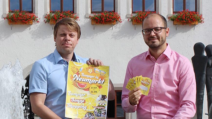 Christian Eisner (aktives Neumarkt) und Matthias Auhuber (Stadtquartier NeuerMarkt) präsentieren das Plakat zur Sommer-Aktion „Sommer | Sonne | Shopping“