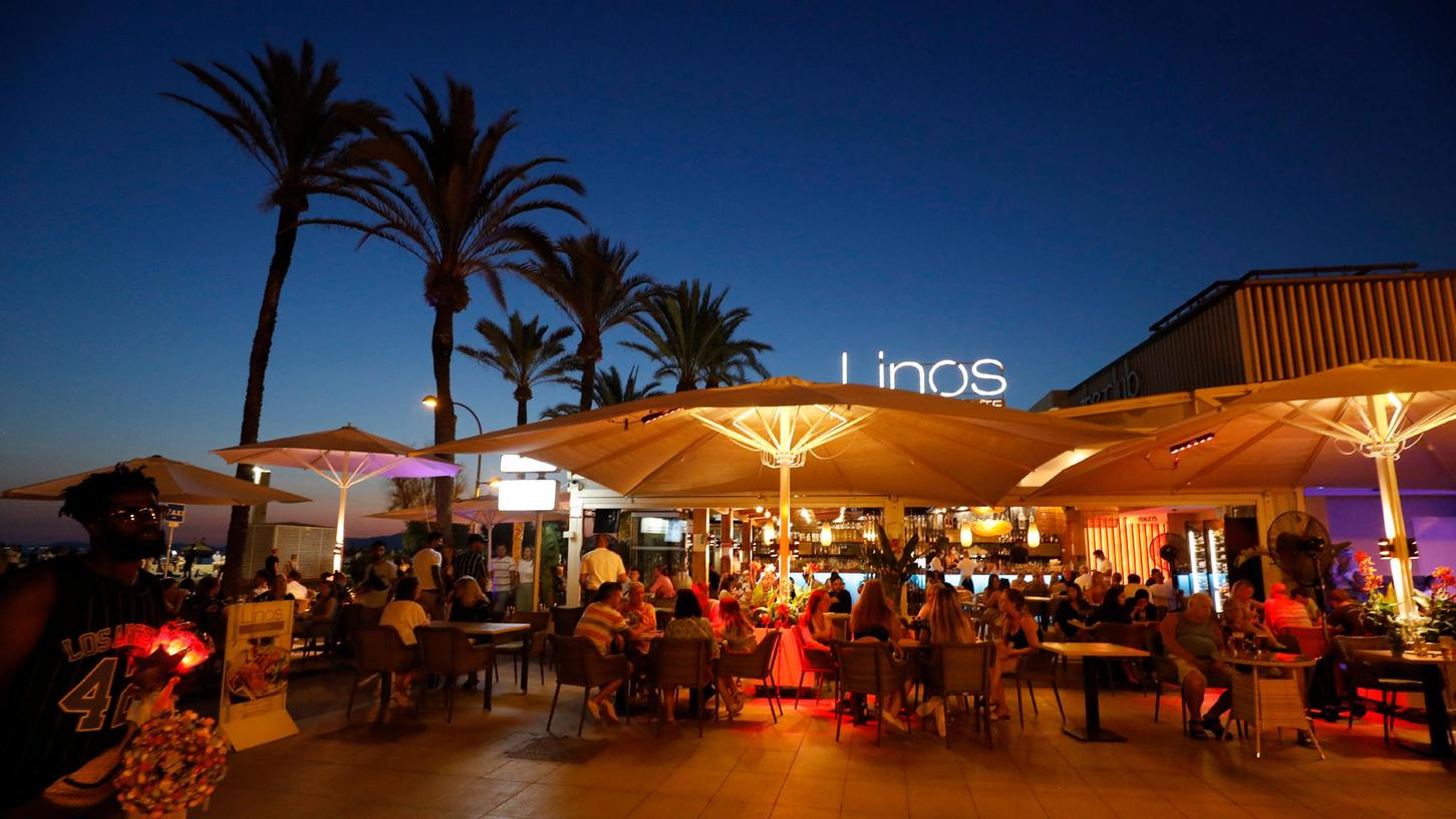 Es könnte alles so schön sein: Menschen sitzen in einer Bar an der Strandpromenade von Palma de Mallorca. Doch die Zahlen der Corona-Neuinfektionen sind auf der Ferieninsel zuletzt heftig gestiegen. Deutschland erklärt ganz Spanien künftig wieder zum Hochinzidenzgebiet.