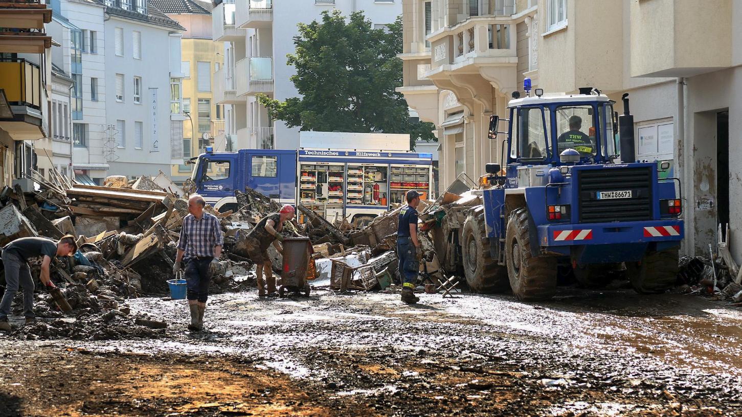  Mitarbeiter des Technischen Hilfswerks (THW) helfen bei Aufräumarbeiten nach der Unwetterkatastrophe in einer verschlammten Straße. 
