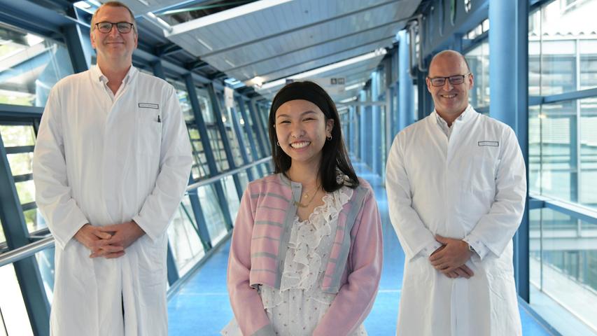 Prof. Dr. Andreas Mackensen (Direktor/Medizin 5, l.) und Prof. Dr. med. univ. Georg Schett (Direktor/Medizin 3, r.) freuen sich mit ihrer Patientin Thu-Thao V. darüber, dass die Therapie mit CAR-T-Zellen so gut bei ihr angeschlagen hat.
