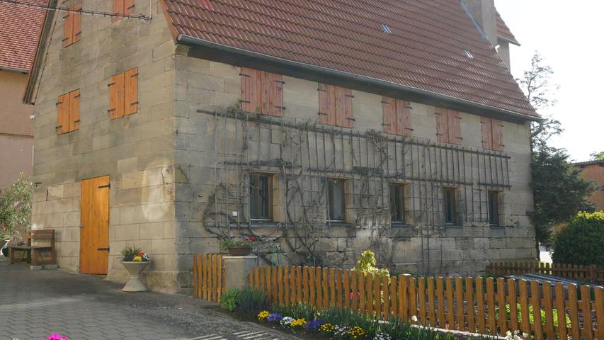 Das Dorfbild entlang der Hauptstraße ist geprägt durch zahlreiche Sandsteingebäude, wie diese liebevoll renovierte Scheune mit Gemüsegarten zeigt.