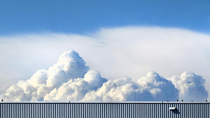 Wie Sahnehäubchen erhebt sich ein Wolkengebirge über einem Hangar des Nürnberger Flughafens.
