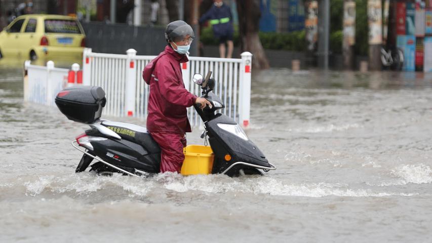 China, Xiamen im August 2021: Ein Motorradfahrer steht mit seinem Fahrzeug im Hochwasser auf einer Straße, nachdem starke Regenfälle in der Provinz Fujian im Südosten des Landes für Überschwemmungen gesorgt haben. Die Regierung veranlasste Notfallmaßnahmen. Weltweit kämpfen Menschen gegen die Folgen des Klimawandels. 