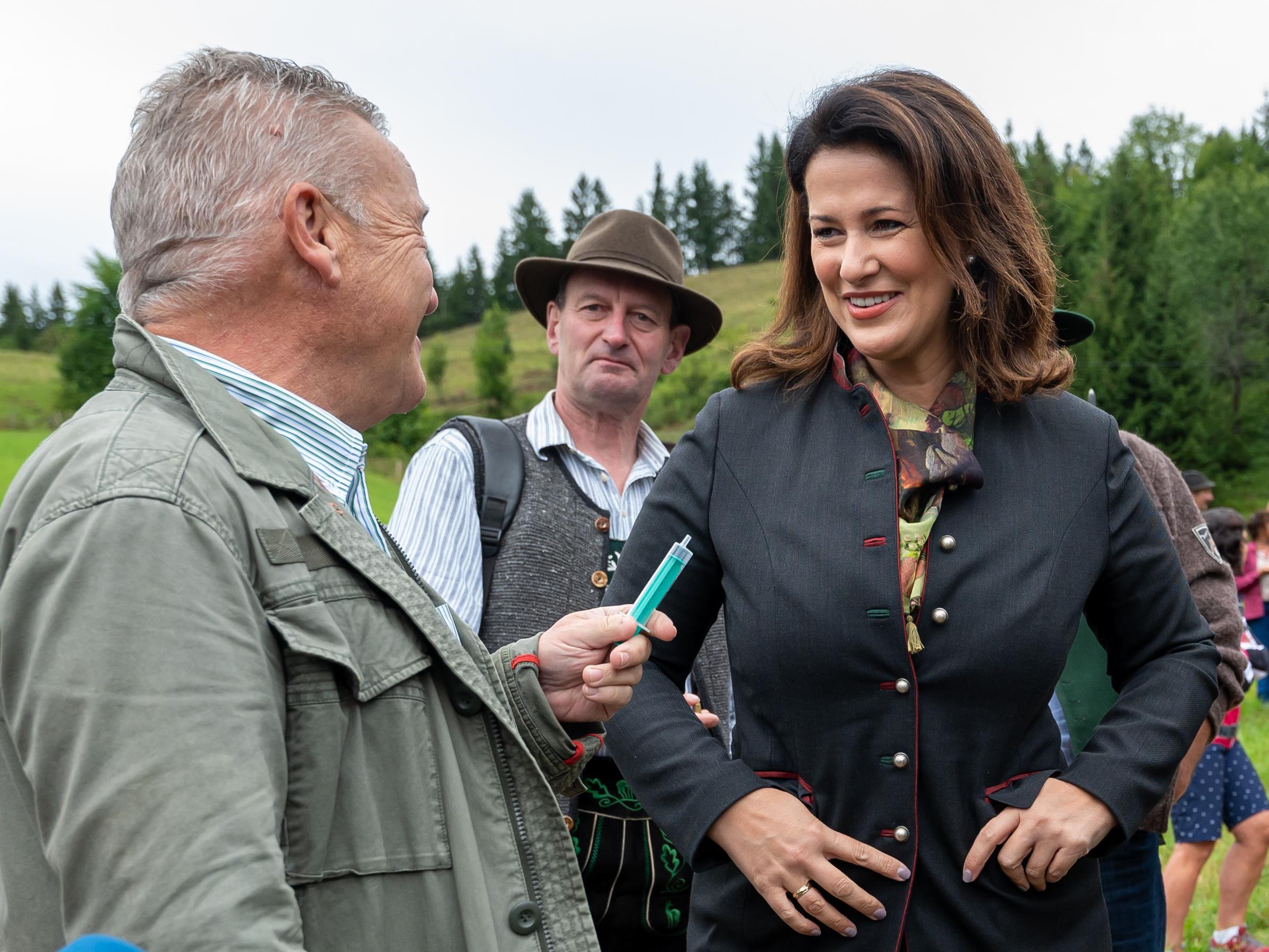Klaus Steiner, CSU-Landtagsabgeordneter, zeigt Michaela Kaniber (CSU), Staatsministerin für Ernährung, Landwirtschaft und Forsten, während der Hauptalmbegehung eine Einwegspritze (befüllt mit Radler), die er zuvor dem stellvertretenden Ministerpräsidenten und Staatsminister für Wirtschaft, Landentwicklung und Energie, Aiwanger (Freie Wähler), angeboten hatte. Der stellte sich mit kritischen Äußerungen zu Coronaimpfungen ins Abseits und lehnte die Annahme der Spritze ab.