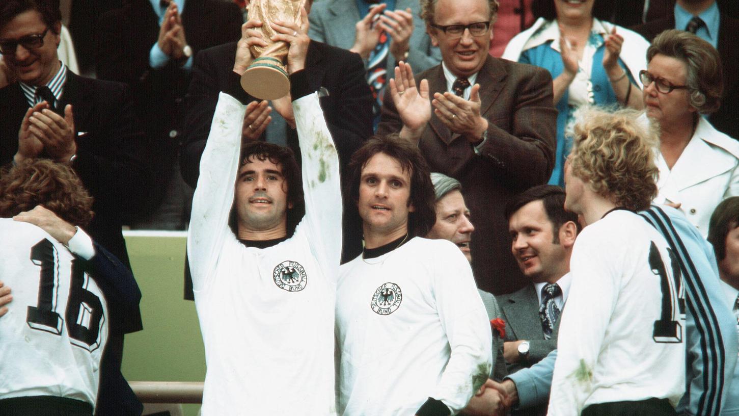 Gerd Müller (links) streckt nach dem Sieg der Fußball-WM 1974 den Pokal in die Luft. Die Fußball-Legende war am Sonntag verstorben. 
