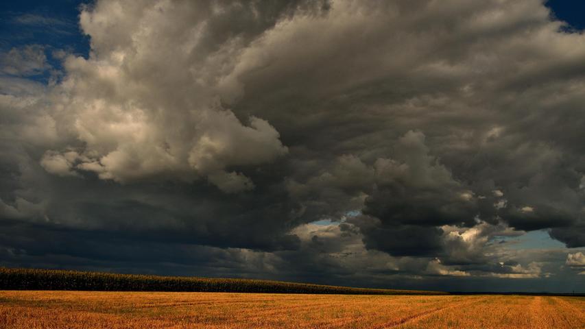 Die Sonnenstrahlen bilden einen schönen Kontrast mit den aufkommenden Regenwolken über einem abgeernteten Getreidefeld und deuten auf ein Wetterwechsel hin.