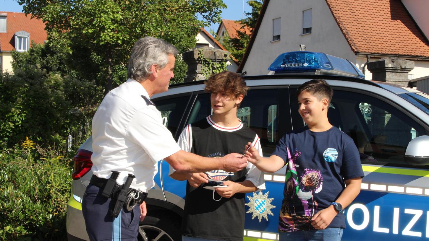 Der stellvertretende Dienststellenleiter Marco Lenz zeigt Fabio Klinger (13, rechts) und Luca Scoccimarro (15) die Polizeiinspektion Gunzenhausen. Im Hof überreichte er ihnen zudem einen Gutschein für einen Onlineshop.