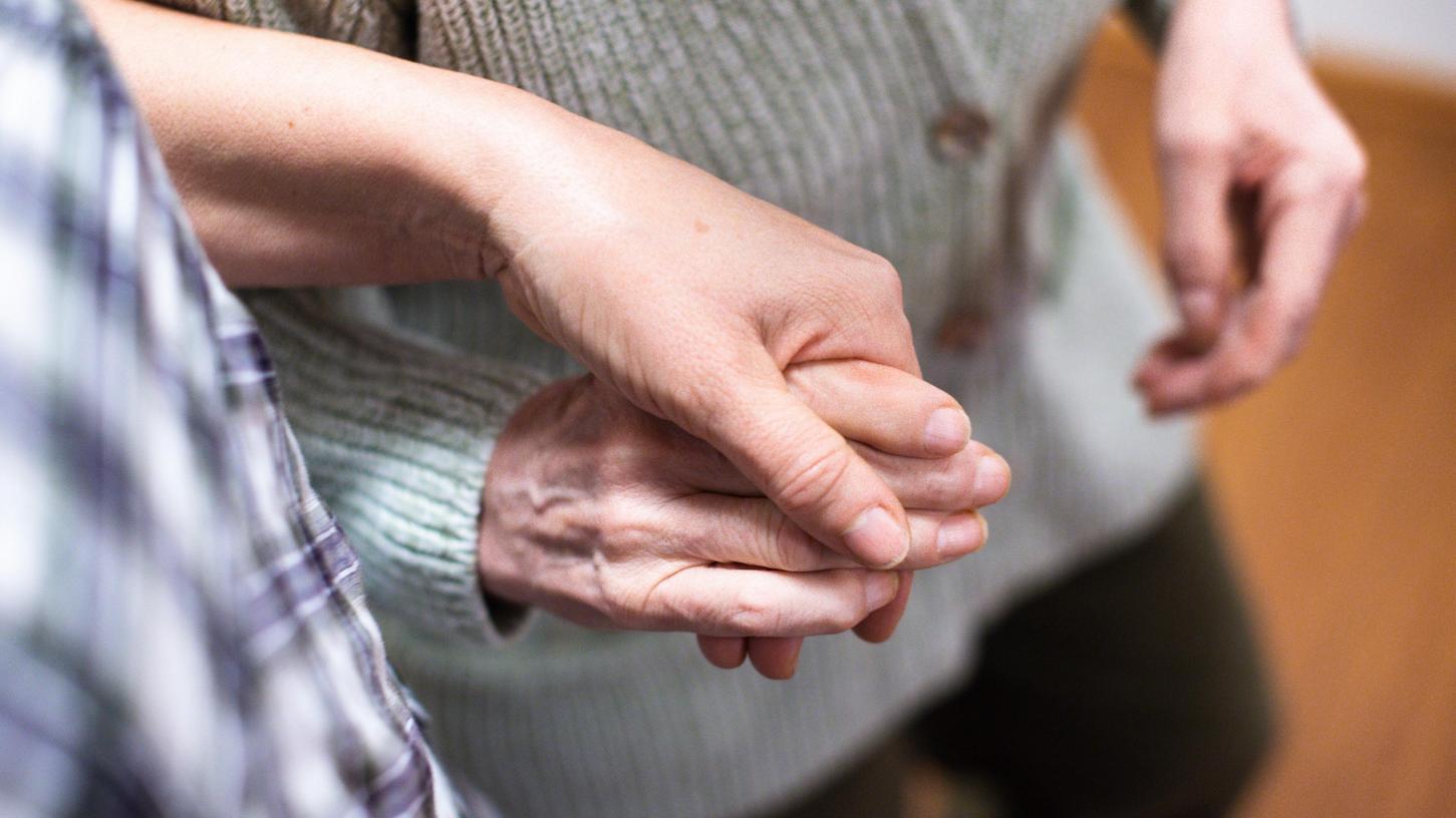 Eine Pflegerin hält die Hand einer Frau im Altenheim. 