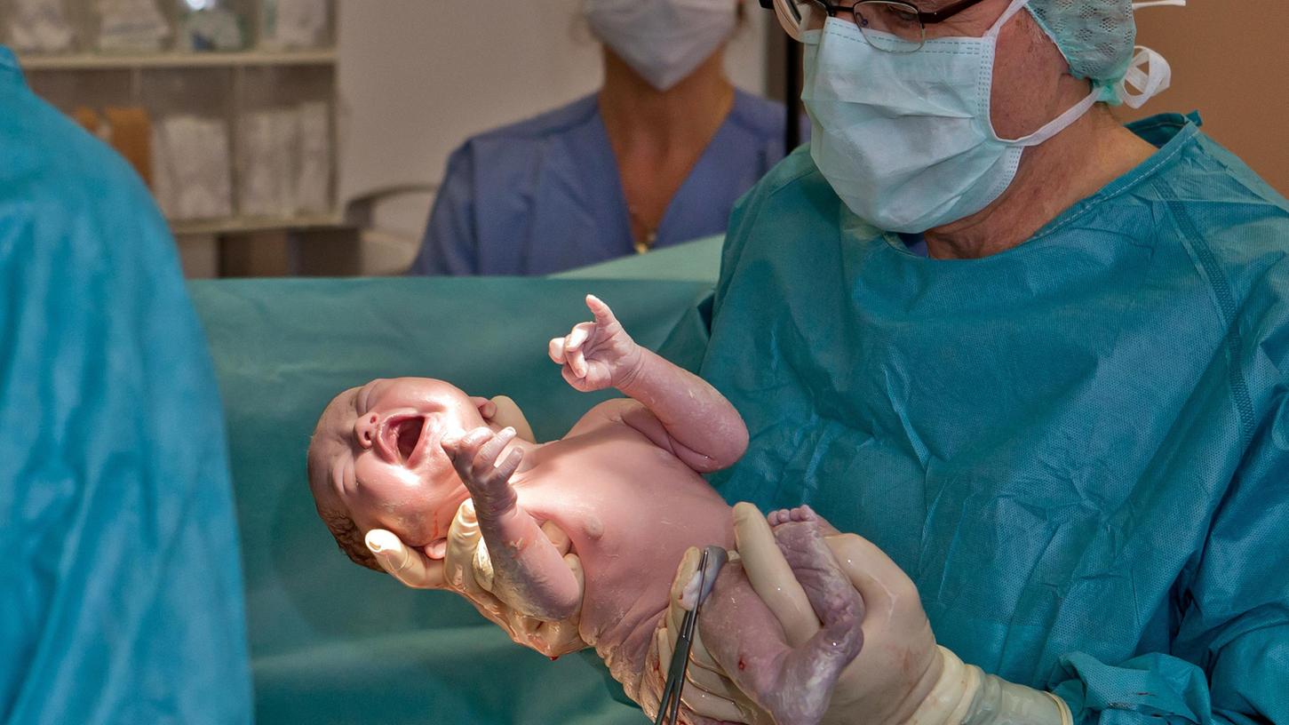Der Oberarzt Mathias Winkler hält ein Baby, das gerade per Kaiserschnitt geboren worden ist, in den Händen. Es kam im Kreißsaal der Geburtshilfe am Uniklinikum Erlangen zur Welt. 
