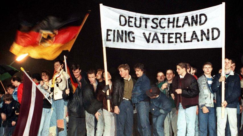 Einheitsübungen am 22. Dezember 1989 auf der Berliner Mauer: Eine Flagge mit Bundesadler trifft auf ein Textzeile aus der DDR-Hymne.
