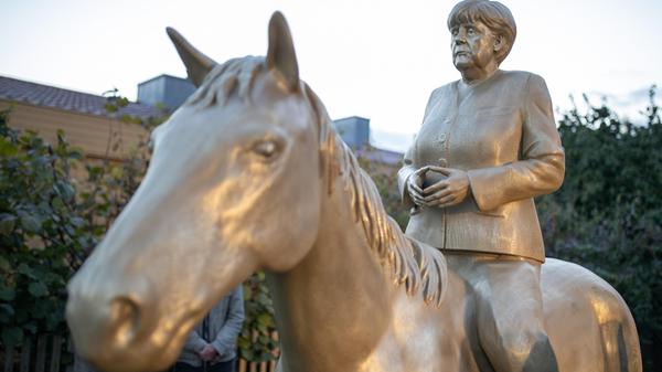 Zum Ende der Ära Merkel überschlagen sich Medien mit Hommagen wie Bilanzen. Sehr viel handfester ist ein Beitrag in der Oberpfalz. Dort dürfte ab sofort das weltweit einzige Reiterstandbild von Angela Merkel stehen. Der Amberger Wilhelm Koch hat der Kanzlerin dieses würdigende Denkmal gesetzt. Oder ist es ein ironischer Kommentar? Das weiß man bei dem umtriebigen Künstler, Verleger und Leiter des Amberger Luftmuseums sowie des Tempel-Museums in Etsdorf nie so ganz genau. Fakt ist: Die lebensgroße Kanzlerin ist jetzt enthüllt. In Etsdorf. Hoch zu Ross.