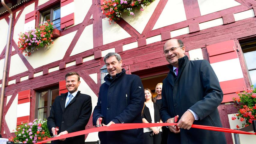 Oberbürgermeister Marcus König, Ministerpräsident Markus Söder und Finanzminister Albert Füracker (v. l.) durchschneiden das rote Band: Das Café ist eröffnet.
