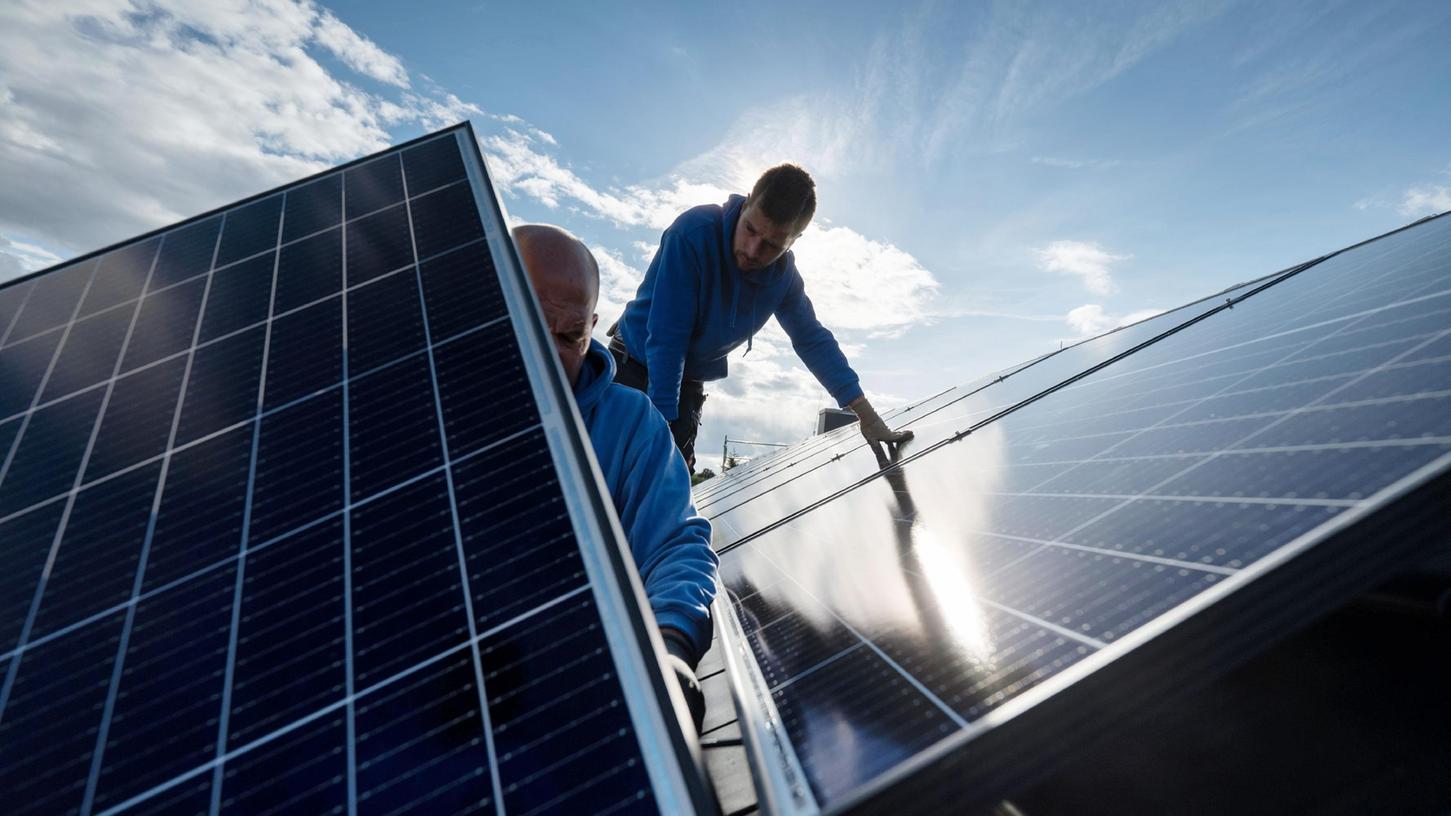 Handwerker montieren Photovoltaikmodule auf dem Dach eines Wohnhauses.

 
