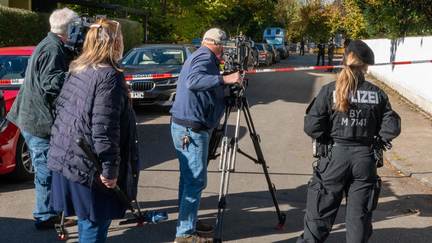 Journalisten und eine Polizistin stehen hinter einer Absperrung der Straße, in der sich der Tatort im Münchner Stadtbezirk Bogenhausen befindet.