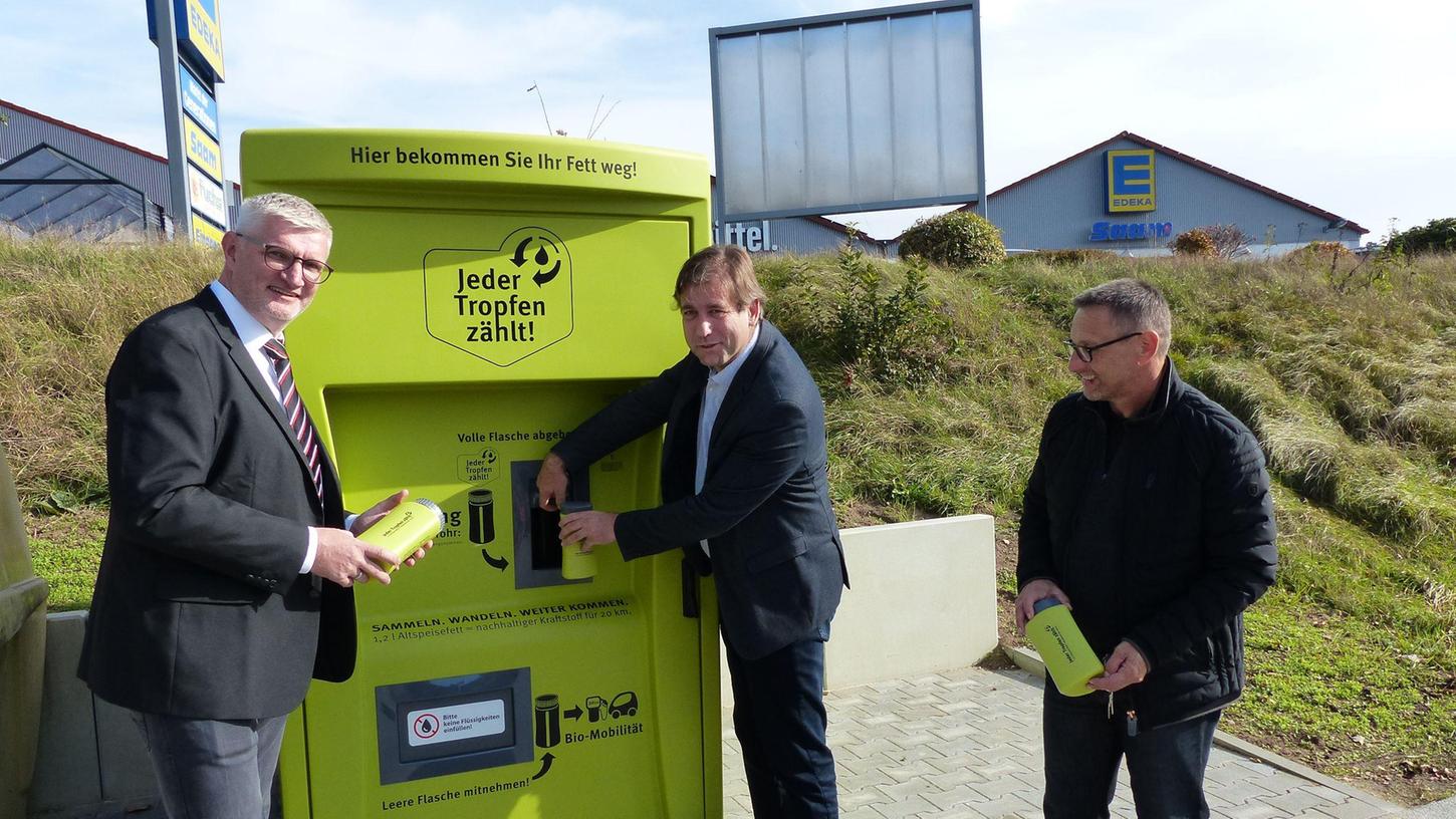 Bürgermeister Ruppert, Landrat Ulm und Hubert Zenk von „Jeder Tropfen zählt“ testen den Speisefett-Automaten.
 
