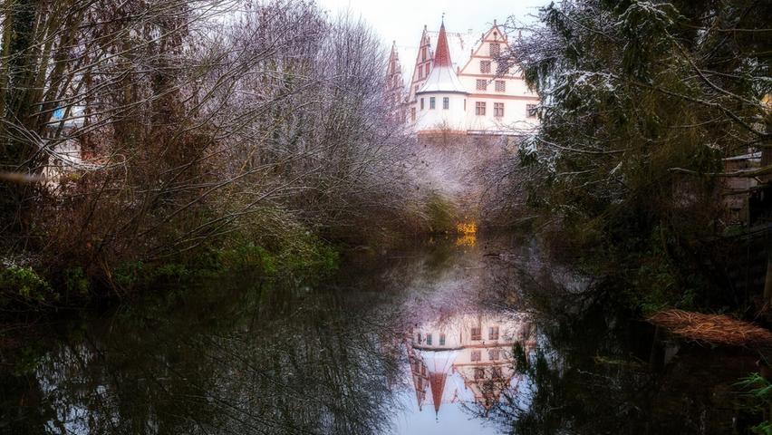 Unter dunklem Tann ein Zauberschloss: Das Schloss Ratibor in Roth spiegelt sich im still daliegenden Rednitzarm.
