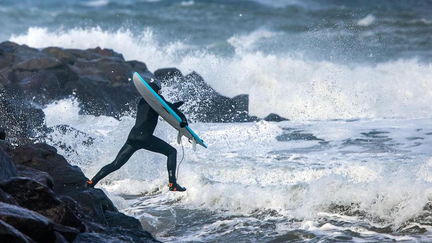 Ein Surfer springt in die eiskalte Ostsee. Bei kräftigem Sturm und hohen Wellen ein aufregendes Schauspiel von Mensch und Natur.