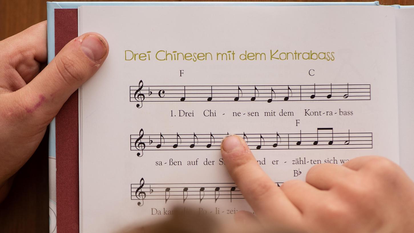 Ein Mädchen hält ein Kinderlieder-Buch in der Hand mit Noten des Liedes "Drei Chinesen mit dem Kontrabass". 