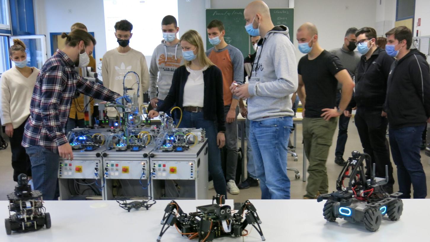 Angehende Wirtschaftsinformatiker und Mechatroniker prüfen an der Berufsschule in Herzogenaurach einen selbst konstruierten und zusammengebauten Logistik-Roboter. Im Vordergrund sind mobile Roboter zu sehen.