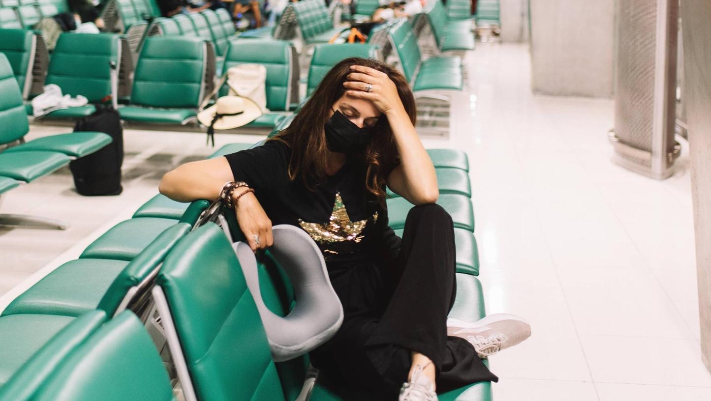 Foto: imago images/Addictive Stock - ..From above of worried young woman with crossed legs wearing mask touching head sitting on chair in airport Copyright: xGabrielxTrujillox
