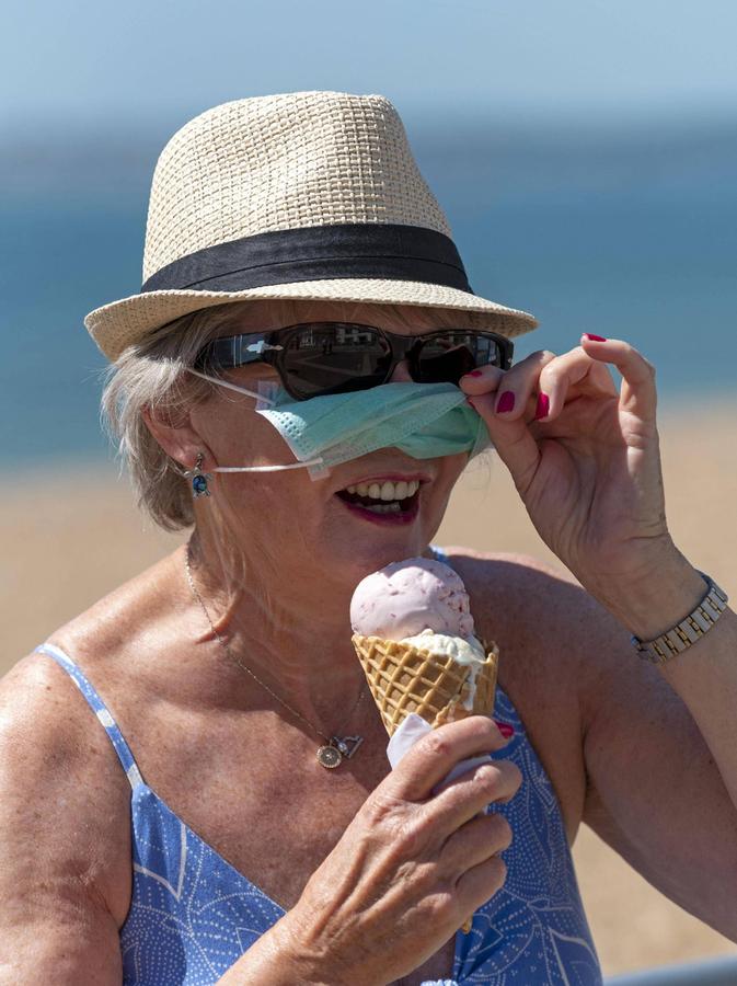 Foto: imago images/UIG - ..Southsea, Portsmouth, Southern England, UK. May 2020. Woman eating ice cream whilst wearing a mask and rubber protective gloves during the Corvid-19 outbreak. On the beach in Southsea. 65197_rf_27_4424-016
