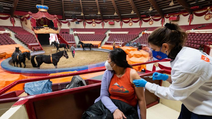 Impfung an der Manege: Impfärztin Caroline Klima (r) impft im Circus Krone Paitul Supaporn gegen das Coronavirus, während im Hintergrund Pferde trainieren.