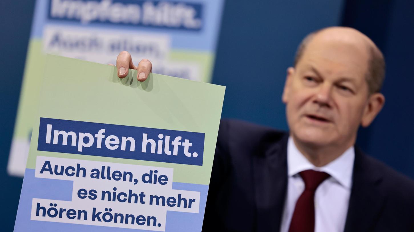 Bundeskanzler Olaf Scholz (SPD) präsentiert ein Plakat für die neue Impfkampagne während der Pressekonferenz.