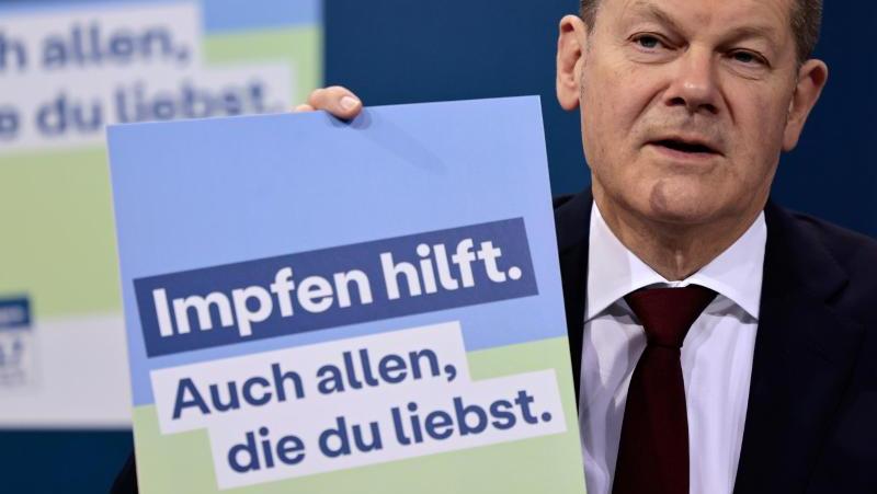 Bundeskanzler Olaf Scholz mit einem Plakat aus der letzten Impfkampagne. Diese stieß bei den Deutschen aber eher auf wenig Anklang. Das Logo erinnert an einen Raststätten-Toilettenanbieter. 
