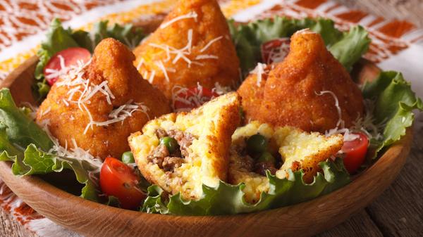 Ein leckerer Snack aus Sizilien und gleichzeitig sogar eines der kulinarischen Wahrzeichen Süditaliens. Die Reiskugeln mit verschiedenen Füllungen werden frittiert. Die wohl bekannteste Variante ist mit Hackfleisch, Erbsen und Mozzarella gefüllt, aber es gibt auch vegetarische Varianten.