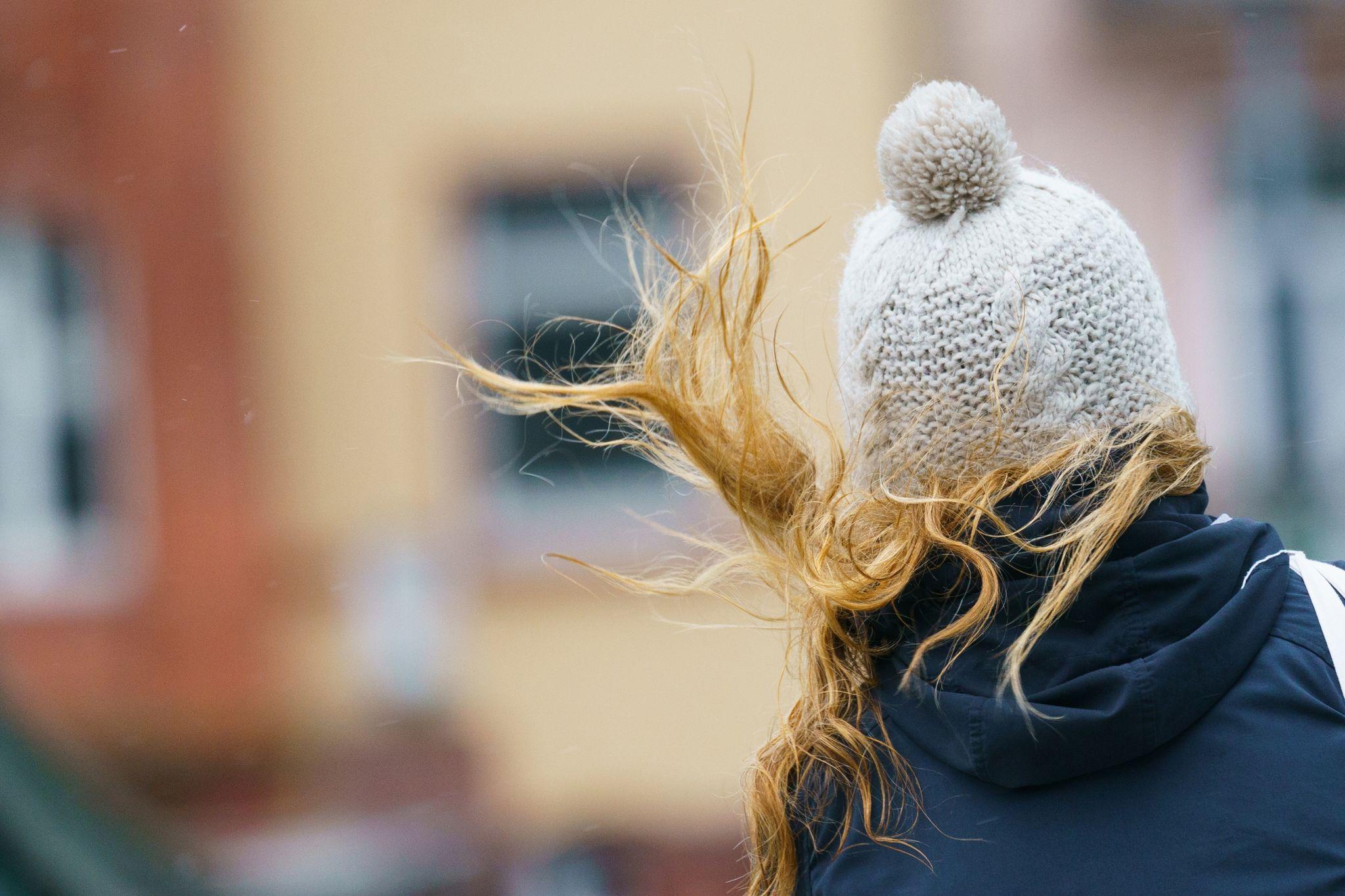 Ein Frau draußen mit Mütze und fliegenden Haaren von hinten.