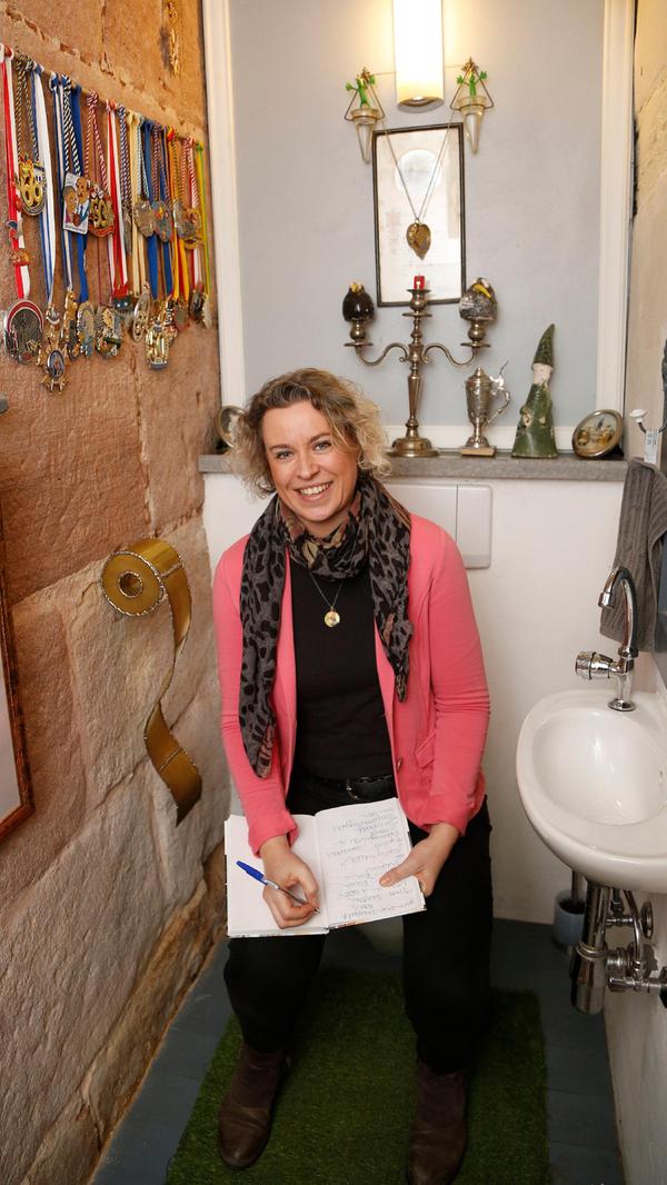 Zum Schluss macht auch Redakteurin Anette Röckl noch einen Witz und posiert mit Schreibwerkzeug auf dem Lokus. Auf die güldene Klopapierrollen-Skulptur fallen übrigens viele immer herein, freut sich der Hausherr.