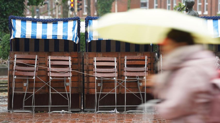 Schleswig-Holstein, Kiel: Passanten gehen im strömenden Regen an verschlossenen Strandkörben eines Gastronomiebetriebs in der Innenstadt vorbei