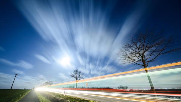 Niedersachsen, Laatzen: Wolken ziehen im Licht des Mondscheins, während Sturmtief Ylenia über die Region Hannover hinwegfegt. Darunter fahren Fahrzeuge über eine Straße