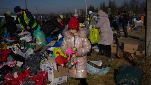 Ein ukrainisches Mädchen steht mit einem Spielzeug in der Hand neben einem Stapel gespendeter Kleidung am Grenzübergang.